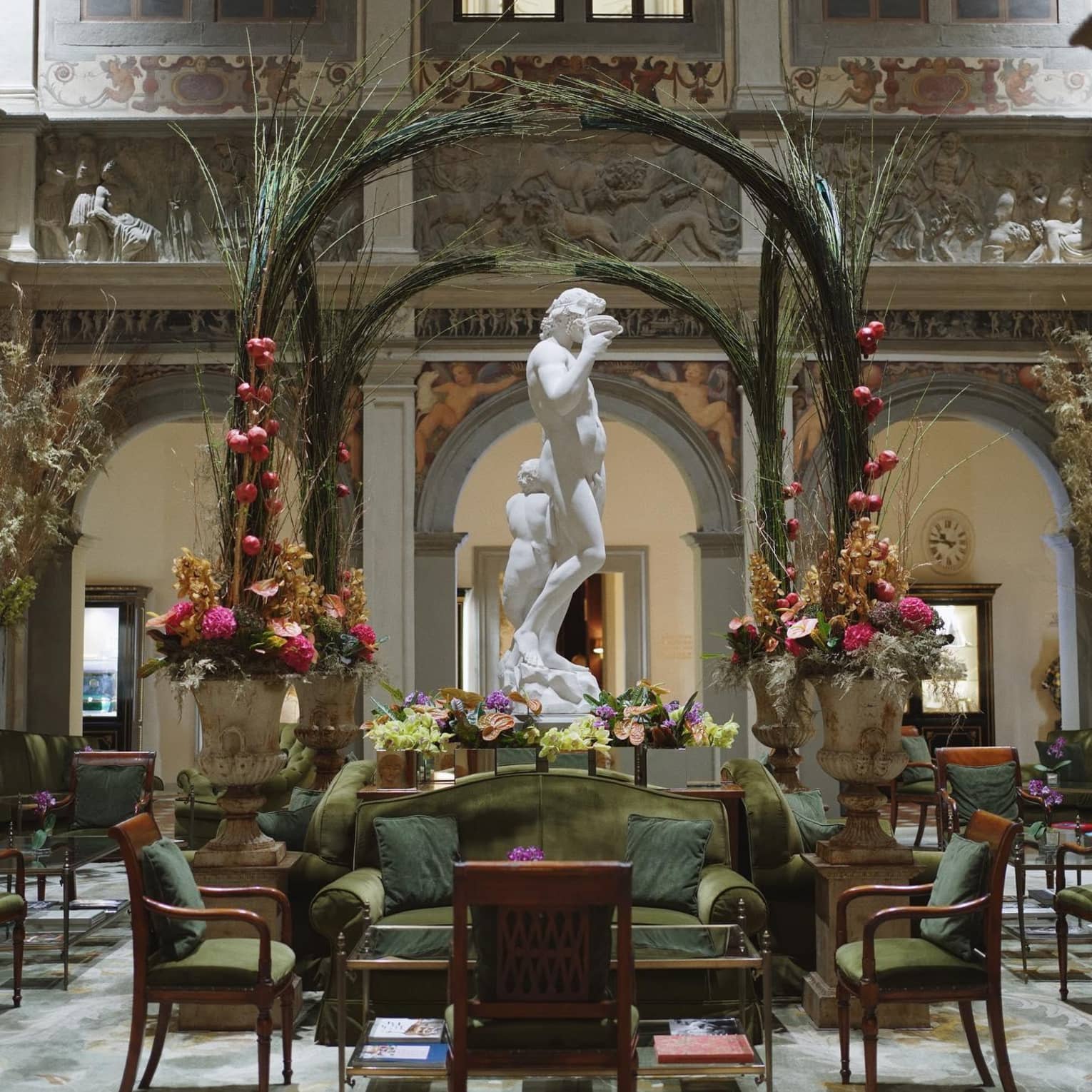 Opulent interior with a white marble statue, green seating, floral arrangements and decorative arches in a grand hall with detailed wall carvingss.
